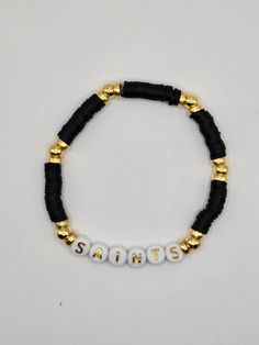 New Orleans Saints Stretch Bracelets made with Black Heishi Beads, Gold Spacers Beads, and Plastic Alphabet Beads. Black Heishi Beads Bracelet With Colorful Beads, Black Beaded Friendship Bracelets With Heishi Beads, Black Heishi Beads Beaded Bracelets, Black Beaded Heishi Friendship Bracelets, Black Heishi Beads Bracelet, Black Bracelets With Letter Beads For Beach, Black Letter Beads Bracelet For Beach, Adjustable Black Heishi Beads Bracelets, Black Beaded Name Bracelet With Round Beads