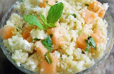 a bowl filled with rice, carrots and mint on top of a wooden table