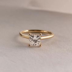 a gold engagement ring with a princess cut diamond in the center on a white surface