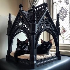 two black cats sitting on top of a bed in front of a stained glass window