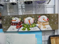 three snowmen sitting on top of a wooden sign