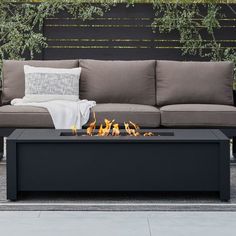 an outdoor fire pit with pillows and blankets on it's sides, in front of a couch