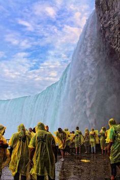 several people in yellow raincoats are standing near a waterfall and looking at the water