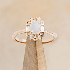 an engagement ring with a white opal surrounded by small diamond cut stones on a wooden stand