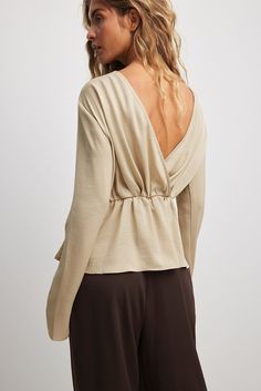 This blouse features a soft smooth touch and a relaxed fit with an elasticized waist. It has a draping design, a deep v backline and an inner silicone trim at the shoulders. This blouse features a flowy bottom hem. Versatile Beige V-neck Blouse, Neutral V-neck Blouse For Fall, Beige Top With Smocked Back For Day Out, Beige Tops With Smocked Back For Day Out, V-neck Top With Smocked Back For Brunch, Elegant V-neck Top With Smocked Back, Draping Design, Draped Blouse, Designer Drapes