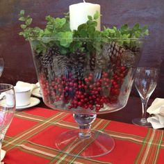 a glass bowl filled with berries and greenery on top of a red table cloth