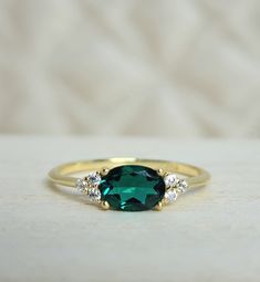 an emerald colored ring with three diamonds on the side and gold band, sitting on a white surface