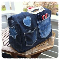 a denim bag with scissors and other items in it sitting on a wooden bench outside