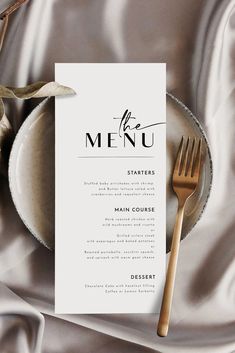 a table setting with a menu and silverware on it, next to a leafy branch