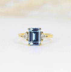 A delicate three stones art deco engagement ring in yellow, rose, white gold or platinum. The main emerald cut 1.55ct aquamarine centered in between trilliant cut diamond frame. It is a perfect choice for those who are looking for a dainty engagement ring in 9k/14k/18k Yellow, Rose or White Gold. It is also a great gift for Christmas, Valentine's Day, birthday, anniversary or for celebration for any special occasion. ✯✯ Free UK and USA shipping ✯✯ ✯ ✯ No Custom Charges for USA orders ✯✯  MADE TO Aquamarine Engagement Ring Art Deco, Yellow Gold Aquamarine Ring, Emerald-cut White Gold Aquamarine Ring, Art Deco Aquamarine Blue Ring, Blue Aquamarine Emerald-cut Diamond Ring, Celebrity Rings, Emerald Cut Diamond Engagement Ring, Dainty Engagement Rings, Emerald Engagement Ring Cut