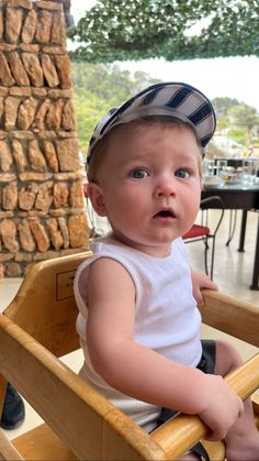 a little boy sitting in a wooden chair with a hat on top of his head