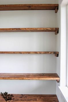 three wooden shelves in the corner of a room with white walls and wood flooring