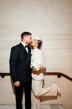 a bride and groom kissing in front of a wall