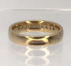 a yellow gold wedding ring with diamonds on the inside and outside, sitting on a clear surface