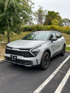 a silver car parked in a parking lot next to trees and grass on a cloudy day