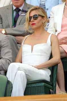 a woman sitting in a chair at a tennis match wearing sunglasses and a white dress