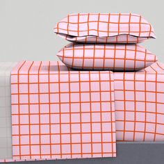 three pillows are stacked on top of each other with orange and white plaid sheets in the background