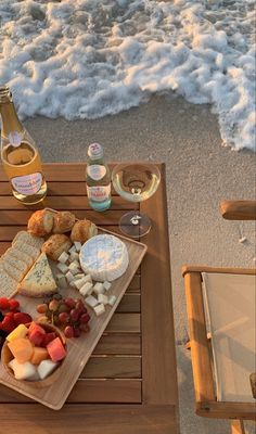 a wooden table topped with cheese and fruit next to the ocean on top of a sandy beach