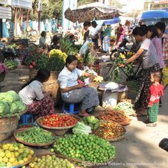 people are shopping at an outdoor market with many fruits and vegetables in baskets on the ground