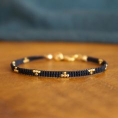 a black bracelet with gold beads on it sitting on top of a wooden table next to a blue pillow