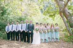 a group of people standing next to each other in front of some trees and bushes