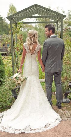 a bride and groom holding hands while standing in front of some bushes at their wedding