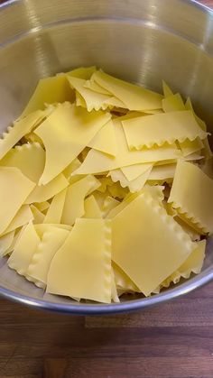 a metal bowl filled with pasta on top of a wooden table