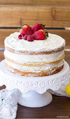 a white cake with strawberries on top sitting on a table next to lemons