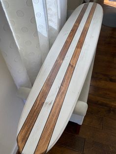 a white and brown surfboard sitting on top of a wooden floor next to a window