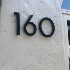 a house number sign on the side of a white building with an open window and shutters