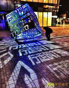 the shadow of a person standing next to a large object with words on it in front of a building