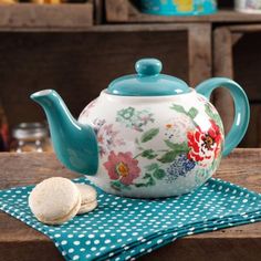 a teapot with flowers painted on it sitting on a table next to some cookies