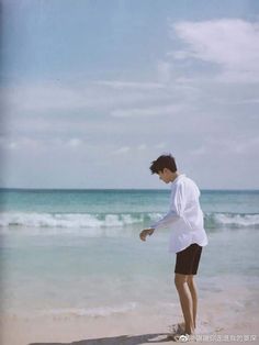 a young man standing on top of a sandy beach next to the ocean holding a frisbee