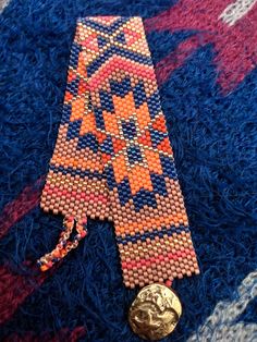 an orange and blue beaded tie laying on top of a rug next to a gold coin