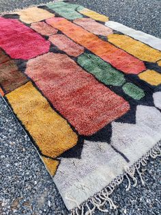 a multicolored rug is laying on the ground with gravel and rocks around it