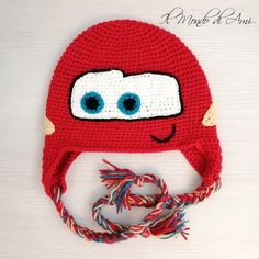 a crocheted red hat with blue eyes and braids on the side, sitting on a white surface