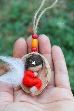 a hand holding a tiny doll in a piece of wood with beads and a star on it