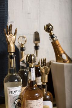 several different types of liquor bottles on a table with gold hand sculptures in the background