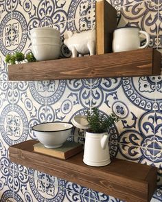 two wooden shelves with pots and bowls on them in front of a blue patterned wall