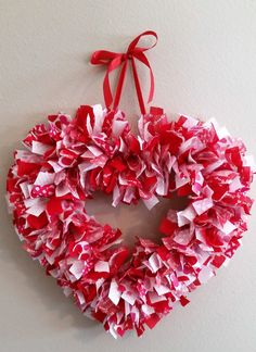 a heart shaped wreath with red and white tissue paper on the front hanging from a wall