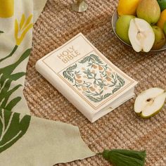 an open book sitting on top of a table next to some apples and pears