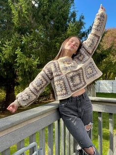 a woman leaning on a rail with her arms up in the air while wearing ripped jeans and a crocheted sweater