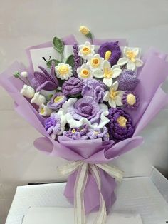 a bouquet of crocheted flowers is wrapped in purple and white paper with a bow