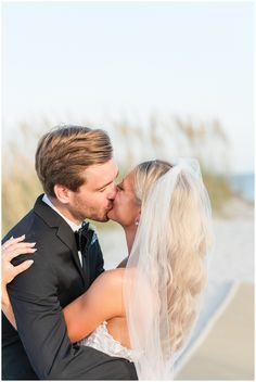 a bride and groom kissing on the beach