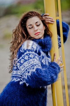 a woman leaning against a yellow pole wearing a blue and white sweater with snowflakes on it