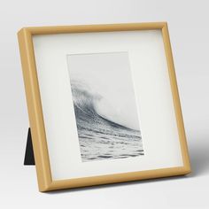 a white and gold frame holds a black and white photo of a wave in the ocean