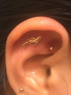 a close up of a person's ear with a small gold bird on it