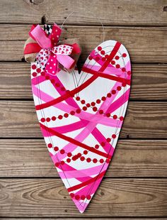 a paper heart hanging on a wooden wall with pink and red ribbons around the edges