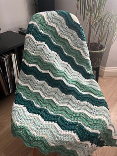 a crocheted blanket sitting on top of a wooden chair next to a potted plant