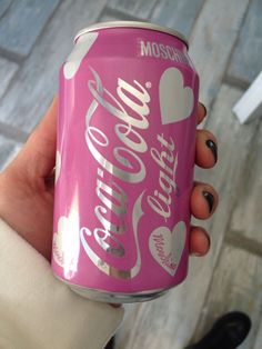 a woman holding a pink can of soda with hearts on the front and bottom, in her left hand